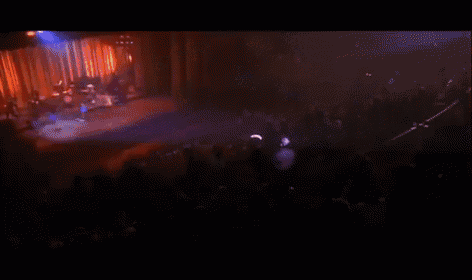 a group of people are dancing on a stage with a drummer in the background