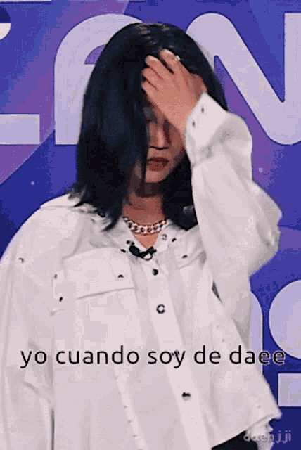 a woman in a white shirt holds her hand to her forehead in front of a sign that says yo cuando soy de daee