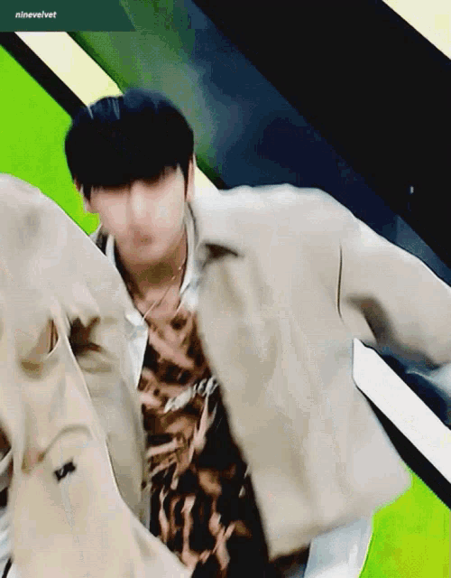 a man in a tan jacket is dancing in front of a green background with ninevelvet written in the corner