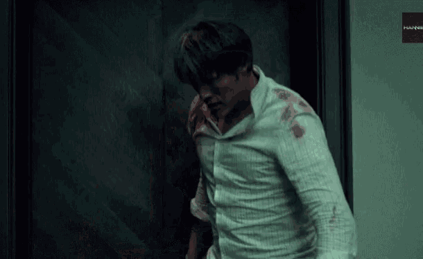 a man with blood on his shirt is walking out of a doorway .