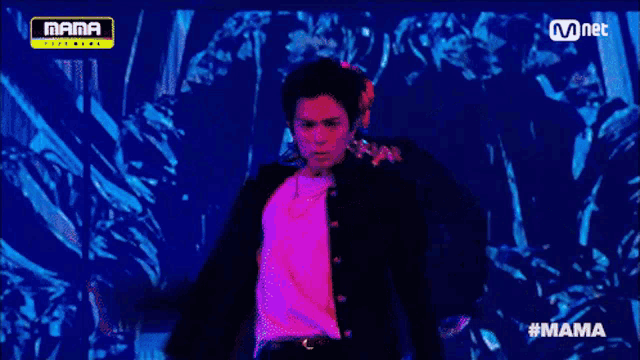 a man in a white shirt and black jacket is dancing on a stage in front of a mnet logo