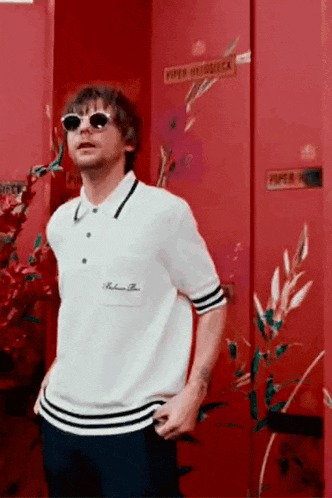 a man wearing sunglasses and a white shirt is standing in front of a red door .