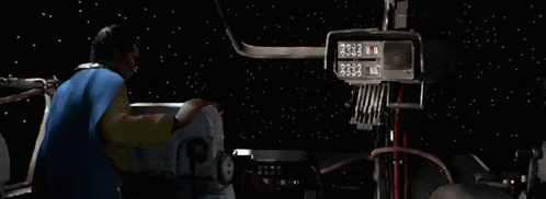 a man in a cape stands in a cockpit of a space ship looking up at the stars