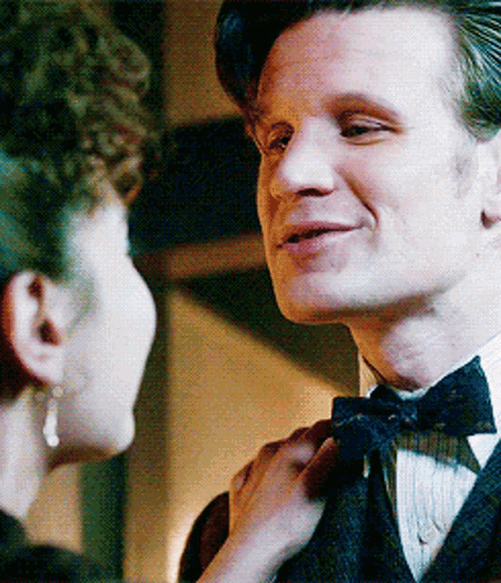 a man and a woman are looking at each other and the woman is adjusting the man 's tie