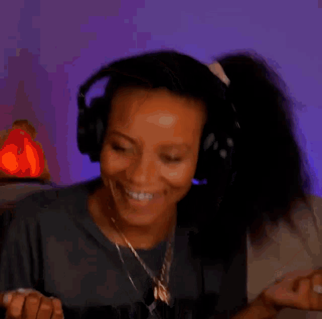a woman wearing headphones and a necklace is smiling and looking at her phone .