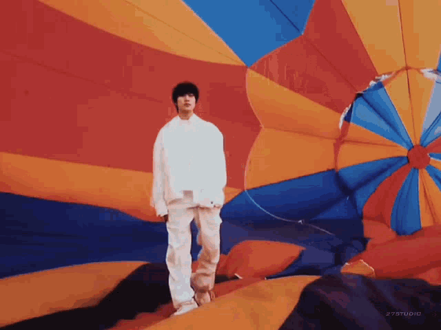 a man in a white shirt is standing in front of a colorful hot air balloon .