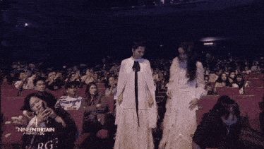 a woman in a white dress stands in front of a crowd of people with the words nineentertainment awards written on the bottom