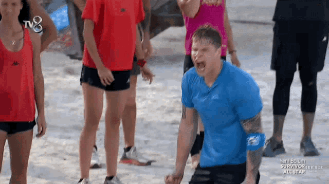 a man in a blue shirt is screaming in front of a group of people who are watching a survivor show