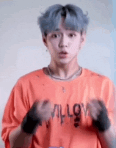 a young man with blue hair is wearing an orange shirt and wristbands and making a funny face .