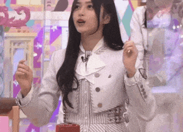 a woman in a white jacket and striped dress is standing in front of a microphone and holding something in her hand .