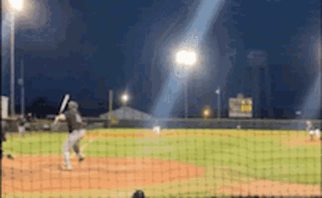 a baseball game is being played at night and a batter is swinging his bat