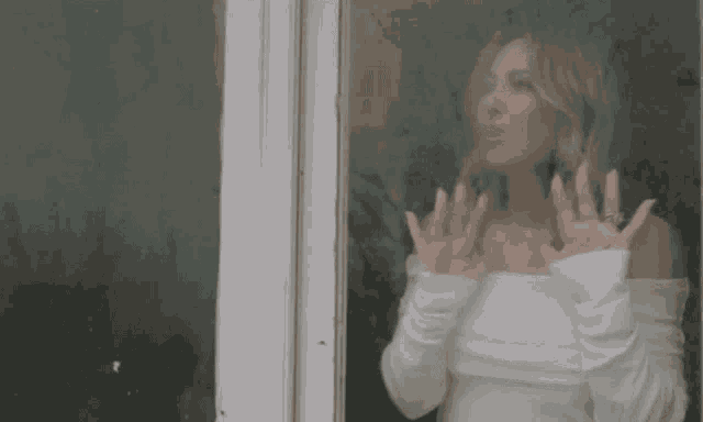 a woman in a white off the shoulder top is looking out of a window .