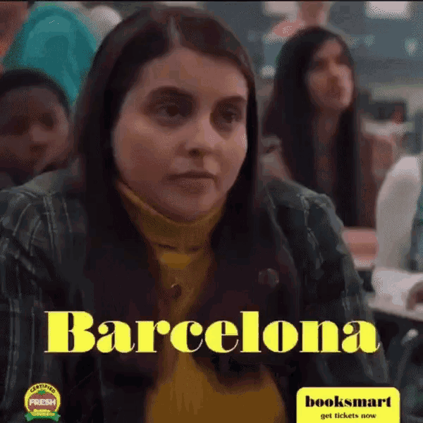 a woman in a yellow turtleneck sits in a classroom with the word barcelona on the bottom right