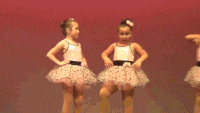 two little girls are dancing on a stage and one has a bow in her hair