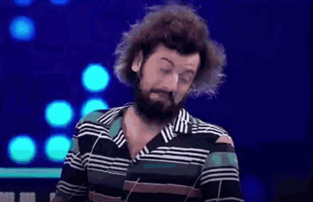 a man with a beard and curly hair is wearing a striped shirt and making a funny face .