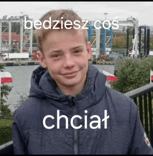 a young boy wearing a jacket with a hood is standing on a bridge .