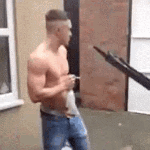 a shirtless man is standing in front of a building holding a cigarette .
