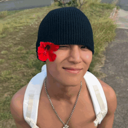a man wearing a black beanie has a red flower on his head
