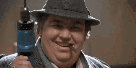 a fat man in a hat is holding a drill in his hand and smoking a cigar .