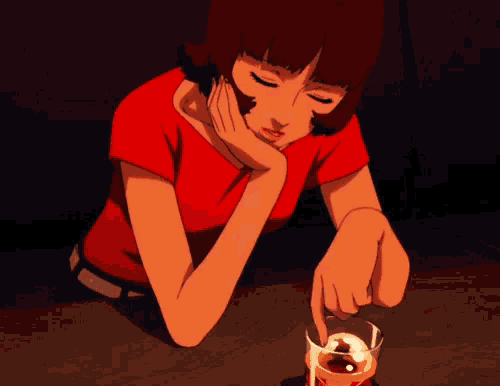 a woman in a red shirt sits at a table with a glass of whiskey in front of her