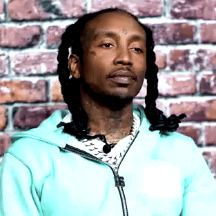 a man with dreadlocks is standing in front of a brick wall wearing a blue jacket .