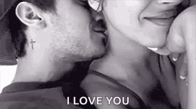 a man and a woman are kissing in a black and white photo . the man has a cross tattoo on his ear .