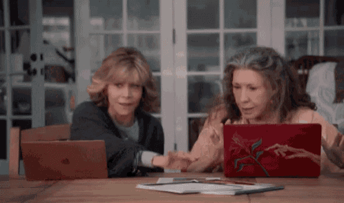 a couple of women are sitting at a table looking at a laptop .