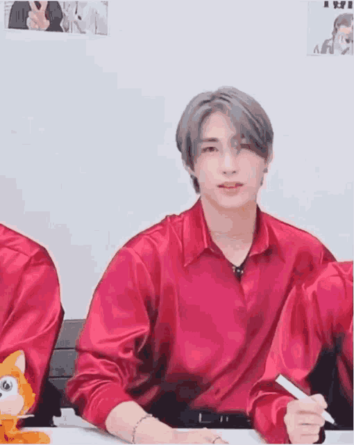 a man in a red shirt is sitting at a table with a pen in his hand and a stuffed animal .