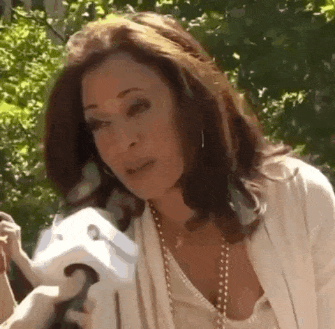 a woman is talking into a microphone while wearing a white shirt and a pearl necklace .