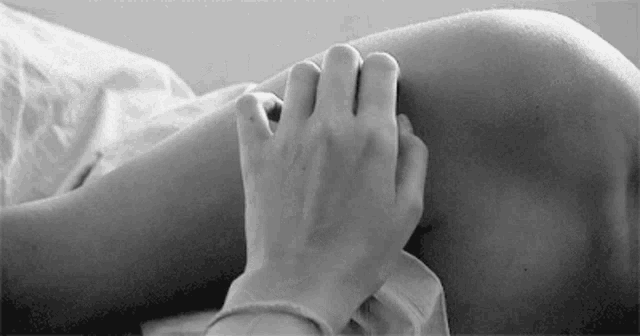 a black and white photo of a person holding another person 's hand on their knee .