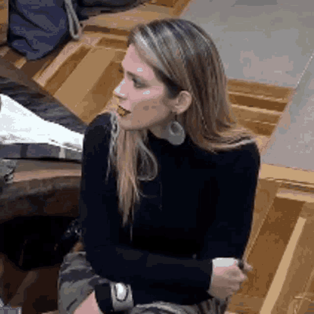 a woman in a black turtleneck is sitting on a wooden floor with her arms crossed .