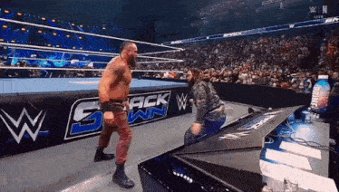 a man is kneeling down in a wrestling ring while another man stands on a table .
