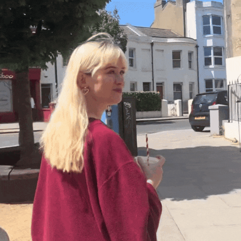 a woman in a red sweater holds a drink with a straw in front of a store called disco