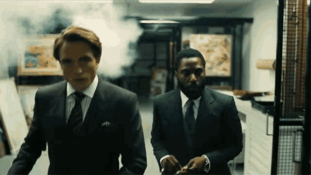 two men in suits are walking down a hallway with smoke coming out of it .
