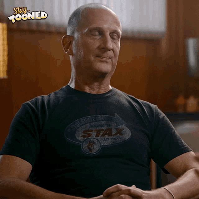 a man wearing a black stax t-shirt is sitting with his eyes closed