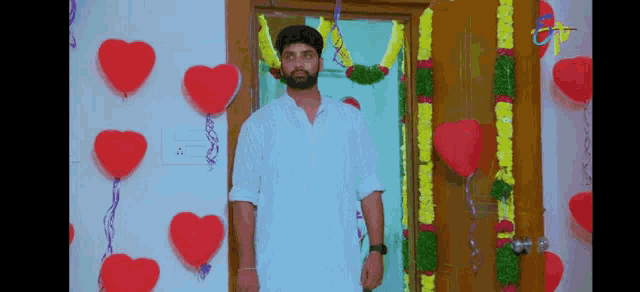 a man in a white shirt is standing in front of a door decorated with hearts and balloons .