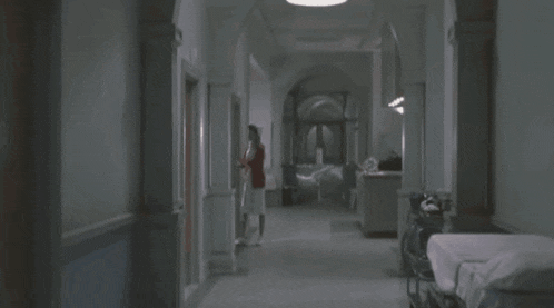 a woman in a white dress is walking down a hallway in a hospital .