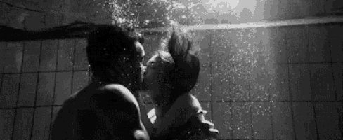 a black and white photo of a man and woman kissing underwater in a swimming pool .