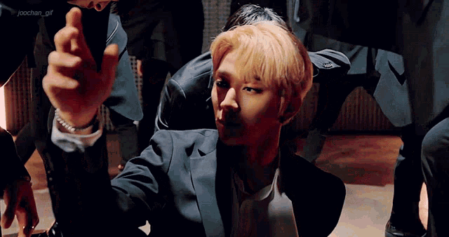 a man in a suit is kneeling down and pointing at the camera