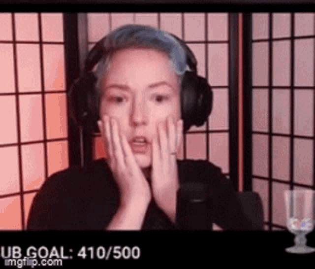 a woman with blue hair is wearing headphones and covering her face with her hands .