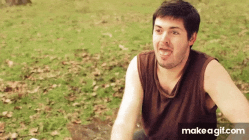 a man is sitting in the grass making a funny face .