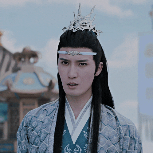 a man with long black hair and a crown on his head looks at the camera