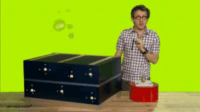 a man in a plaid shirt stands in front of a large box that says les apprentis on it