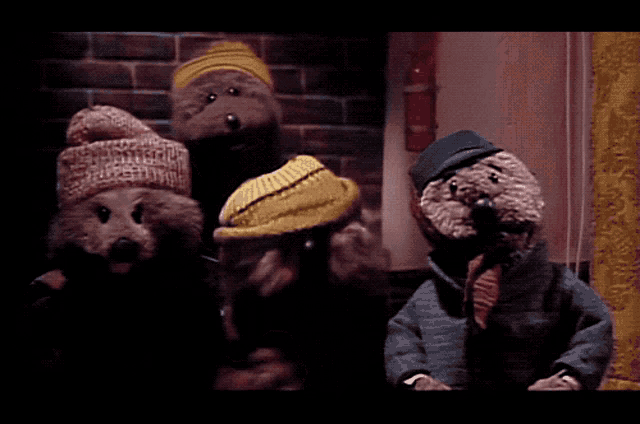 a group of stuffed animals wearing hats and scarves are standing in front of a brick wall