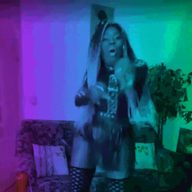 a woman is dancing in front of a couch in a room with purple and green lights