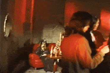 a man in a red sweater is standing next to a woman in a red chair in a dark room