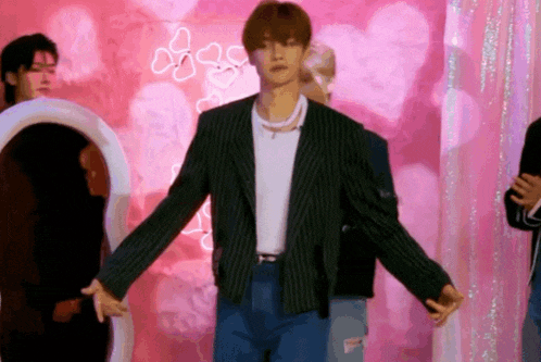 a man in a striped jacket is standing in front of a pink wall with hearts on it .