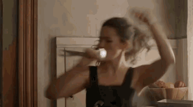 a woman is brushing her teeth with a toothbrush in front of a mirror in a kitchen .