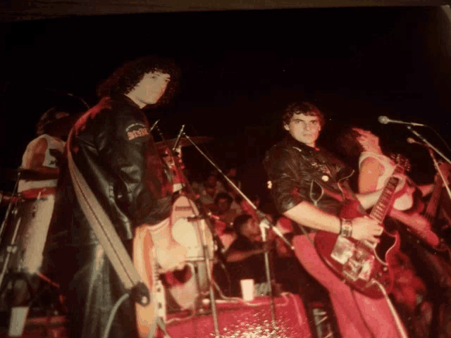 a man in a leather jacket with ac dc on the sleeve is playing a guitar