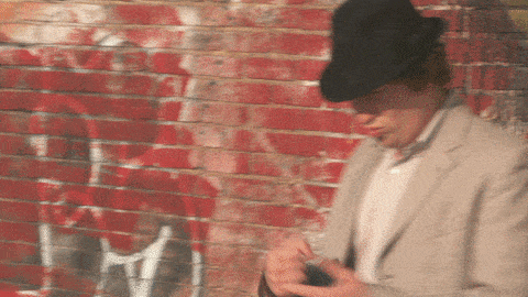 a man wearing a hat is standing in front of a brick wall